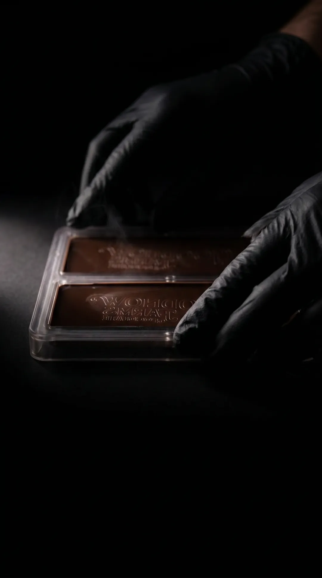 Gloved hands lifting a set chocolate bar mould in low light